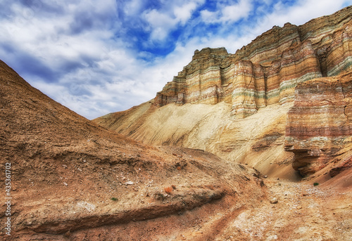 A canyon among the ancient desert steppe fields, geological deposits of different times, clay, erosion, stones. Rocky cliffs, hills and mountains in the Altyn-Emel park in Kazakhstan. Sky with clouds.