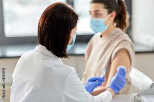 health, medicine and pandemic concept - close up of female doctor or nurse wearing protective medical gloves with syringe vaccinating patient at hospital