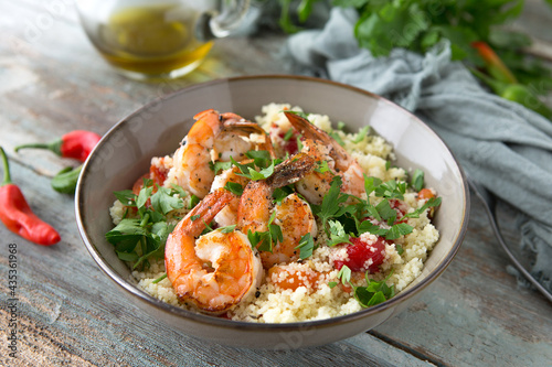 a bowl of couscous with shrimps and chili on a wooden table