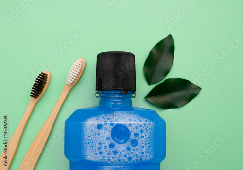 Mouthwash, several leaves, two wooden bamboo toothbrushes on a green background. Flat lay, top view, copy space for text. selective focus