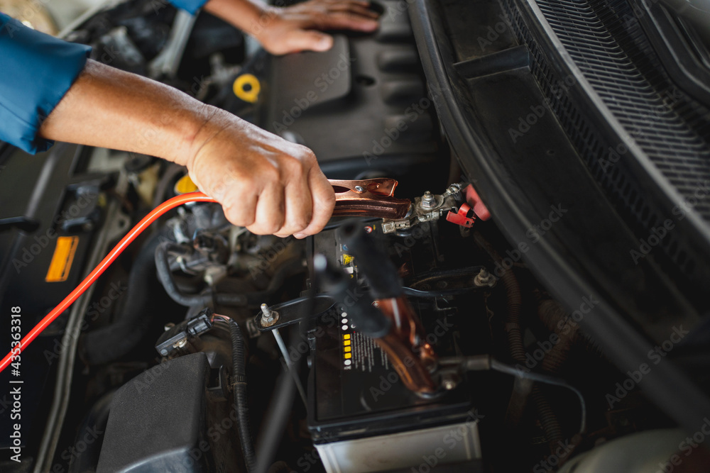 Car mechanic uses a battery jumper cable to charge the dead battery. Car repair service concept.