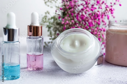 Composition of modern facial skin care, cosmetics, moisturizer and serum on a light marble background, pink flowers in the background. Close-up, horizontal photo