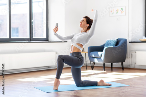 fitness, people and healthy lifestyle concept - young woman with smartphone and earphones doing yoga at home