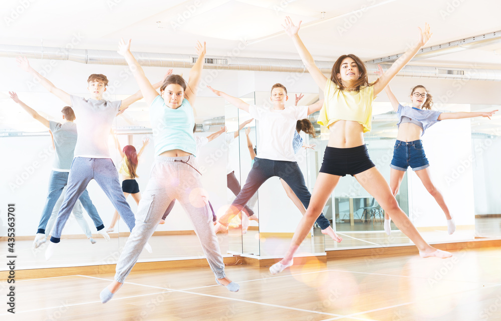 Satisfied teenage boys and girls jumping having fun during dance class