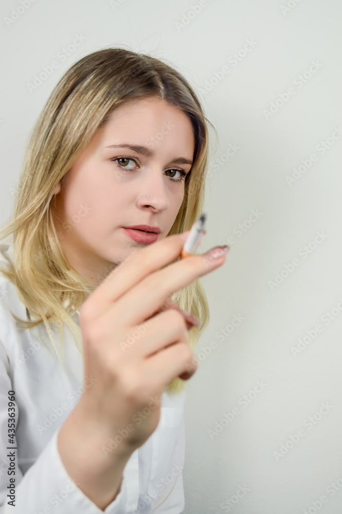 Portrait of a beautiful young blonde woman who is smoking a cigarette and is looking at camera, focus on her face Portrait of a beautiful young blonde woman who is smoking a cigarette and is looking at camera, focus on her face