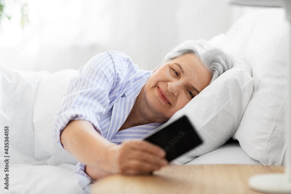 old age and people concept - happy smiling senior woman with smartphone lying in bed at home bedroom old age and people concept - happy smiling senior woman with smartphone lying in bed at home bedroom