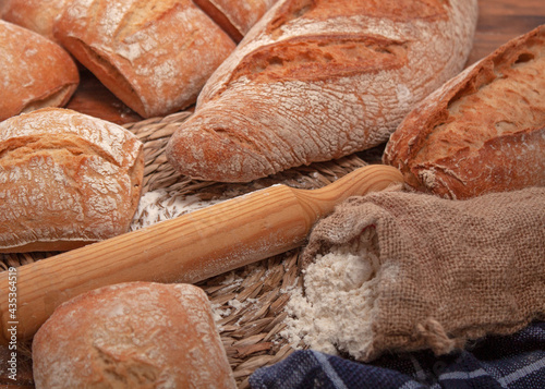 Vista de varios panes alrededor de un mantel de esparto con un rodillo de madera y un pequeño saco de harina