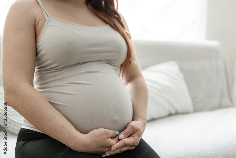 Close-up of a big belly of a pregnant woman in a tank top.