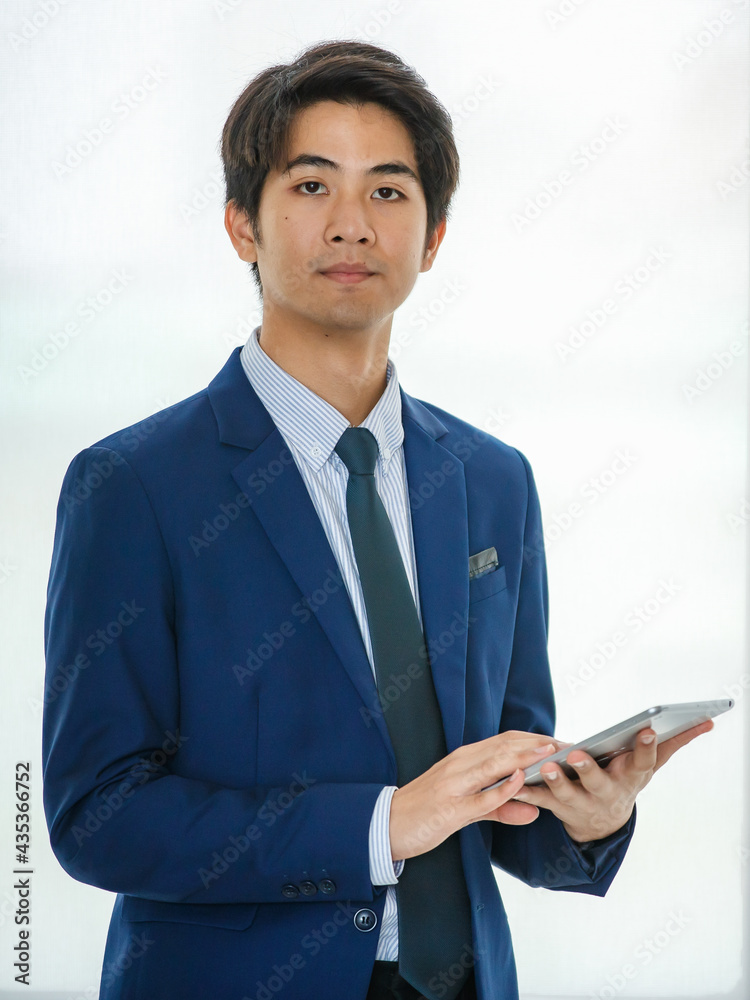 20s young confident attractive Asian businessman wearing formal suit, standing and putting hand in pocket pants, holding tablet and looking at the camera. Showing modernity, startup, and technology. 20s young confident attractive Asian businessman wearing formal suit, standing and putting hand in pocket pants, holding tablet and looking at the camera. Showing modernity, startup, and technology.