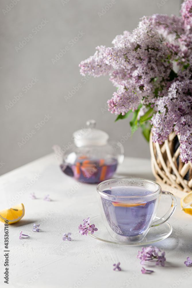Spring composition with a cup of purple tea and lilac flowers on light background. Spring tea party, tea drinking. Menu, lilac tea recipe. Copy space