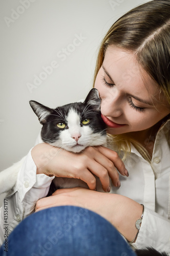 beautiful young blonde woman cuddling a bored looking young black and white cat close up