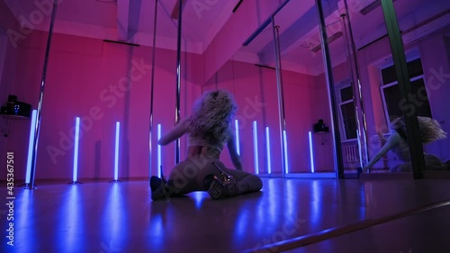 Young woman with slim body dancing using pylon. High heels. Blonde slender female dancing near pole with pink and blue light at background. Exotic dance in 4K, UHD