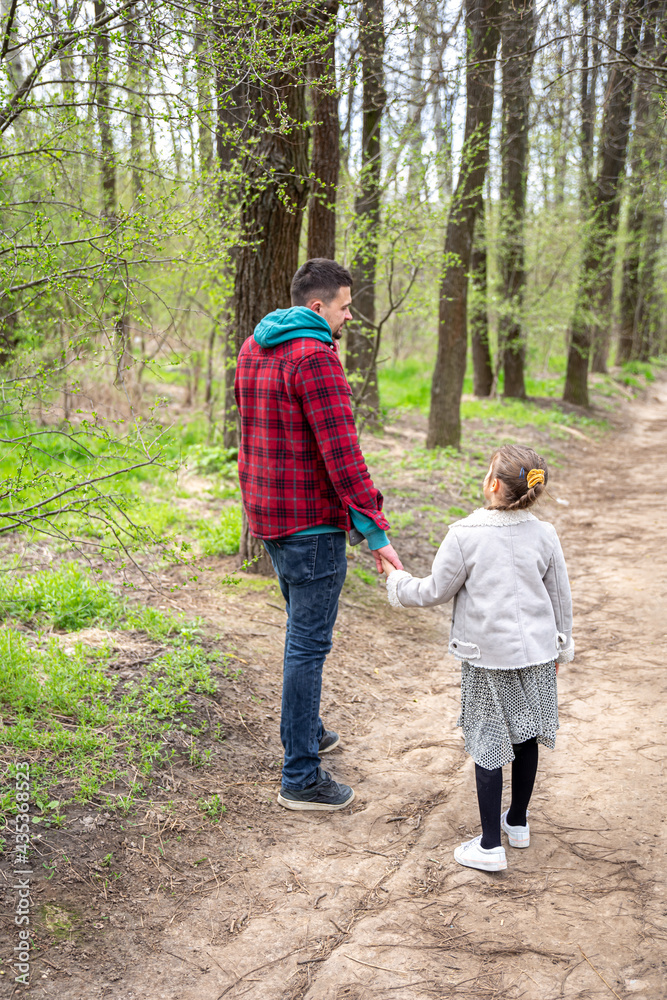 Fototapeta premium Little girl with dad is walking in the spring forest, holding hands.