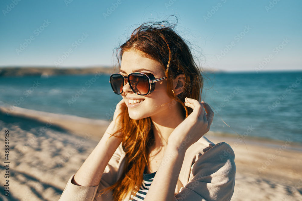 traveler in a beige jacket and sunglasses on the sand near the sea on the beach