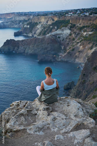 Woman is siting on a rock, looking at the sea landscape, sunset and enjoying the view and fresh air.