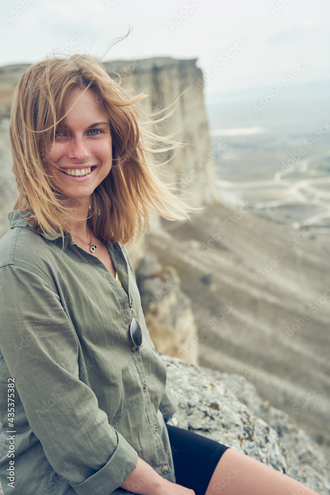 Woman is sitting on the stones, resting, laughting and enjoying the view and fresh air.