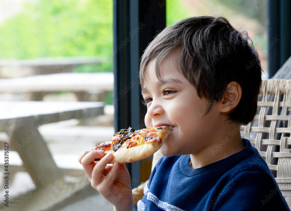 Happy Kid eating home made pizza in the cafe, Cute little Child boy biting off big slice of fresh made pizza in the restaurant, Family happy time concept Happy Kid eating home made pizza in the cafe, Cute little Child boy biting off big slice of fresh made pizza in the restaurant, Family happy time concept