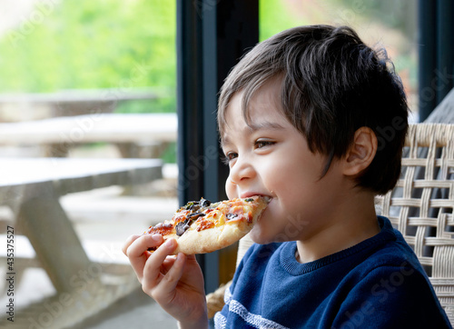 Happy Kid eating home made pizza in the cafe  Cute little Child  boy biting off big slice of fresh made pizza in the restaurant  Family happy time concept