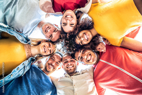 Multiracial group of young people standing in circle and smiling at camera - Happy diverse friends having fun hugging together - Low angle view photo