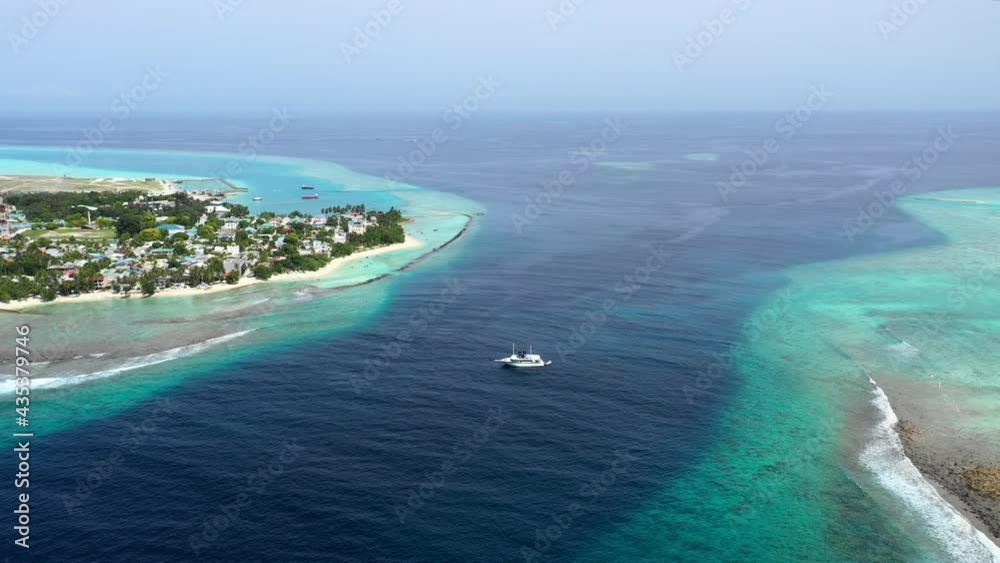 Aerial Panning A Boat Moored Between Two Small Tropical Islands With Deep Blue Sea Stretching To The Horizon Under Bright Sun - Thulusdhoo, Maldives Aerial Panning A Boat Moored Between Two Small Tropical Islands With Deep Blue Sea Stretching To The Horizon Under Bright Sun - Thulusdhoo, Maldives