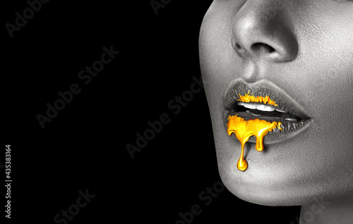 Lipstick dripping. Paint drips, lipgloss dripping from sexy lips, liquid Gold metallic paint drops on beautiful model girl's mouth, creative make-up. Desaturated Beauty woman face makeup close up. Art
