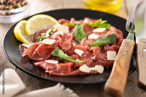 Marbled beef carpaccio on black plate on rustic wooden table