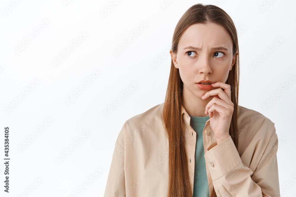 Worried pensive teen student look aside, touching lip nervously and thinking, standing anxious or hesitant against white background Worried pensive teen student look aside, touching lip nervously and thinking, standing anxious or hesitant against white background