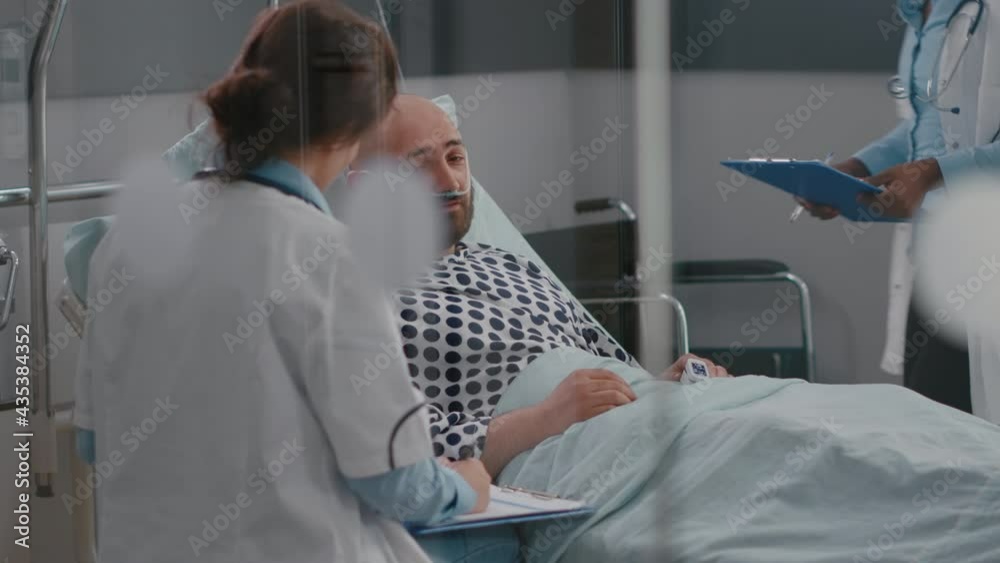 Professional doctors discussing sickness symptom with sick man writing medical tratment on clipboard working in hospital ward. Patient resting in bed while practitioner monitoring disease recovery