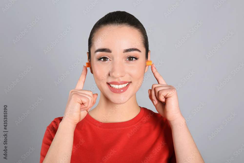 Young woman inserting foam ear plugs on grey background Young woman inserting foam ear plugs on grey background