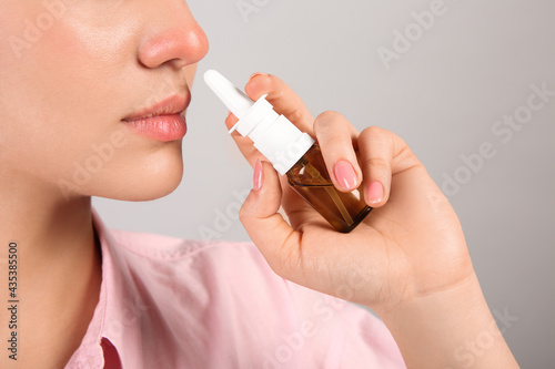 Woman using nasal spray on light grey background, closeup. Space for text