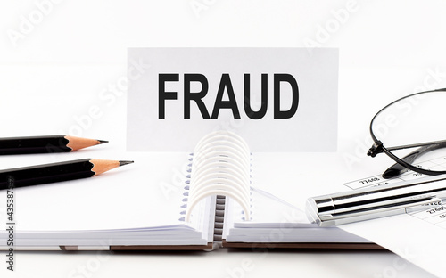 Text FRAUD on paper card,pen, pencils,glasses,financial documentation on table - business concept