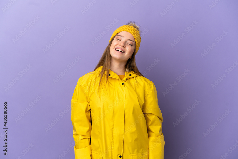 Teenager girl wearing a rainproof coat over isolated purple background laughing Teenager girl wearing a rainproof coat over isolated purple background laughing