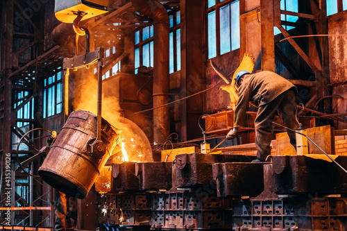 Liquid iron molten metal pouring from ladle container into mold, industrial metallurgical factory, foundry cast, heavy industry background. photo