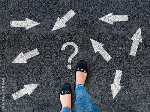 woman in shoes standing on asphalt next to multitude of arrows in different directions and question mark, confusion choice chaos concept 