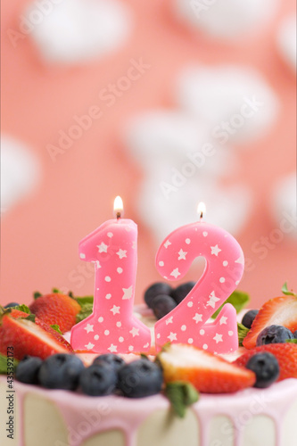 Birthday cake number 12. Beautiful pink candle in cake on pink background with white clouds. Close-up and vertical view © Stanislav
