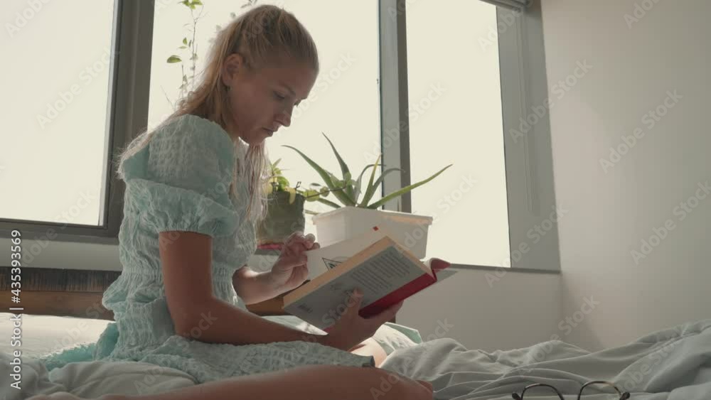 Woman in her bedroom sitting by the window reading a book Woman in her bedroom sitting by the window reading a book