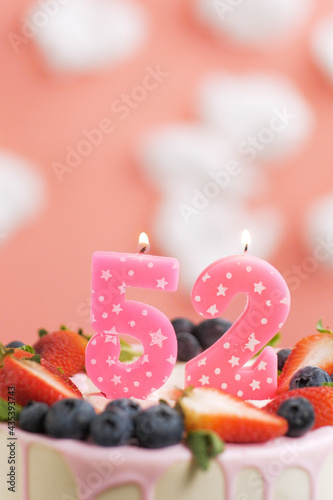 Birthday cake number 52. Beautiful pink candle in cake on pink background with white clouds. Close-up and vertical view