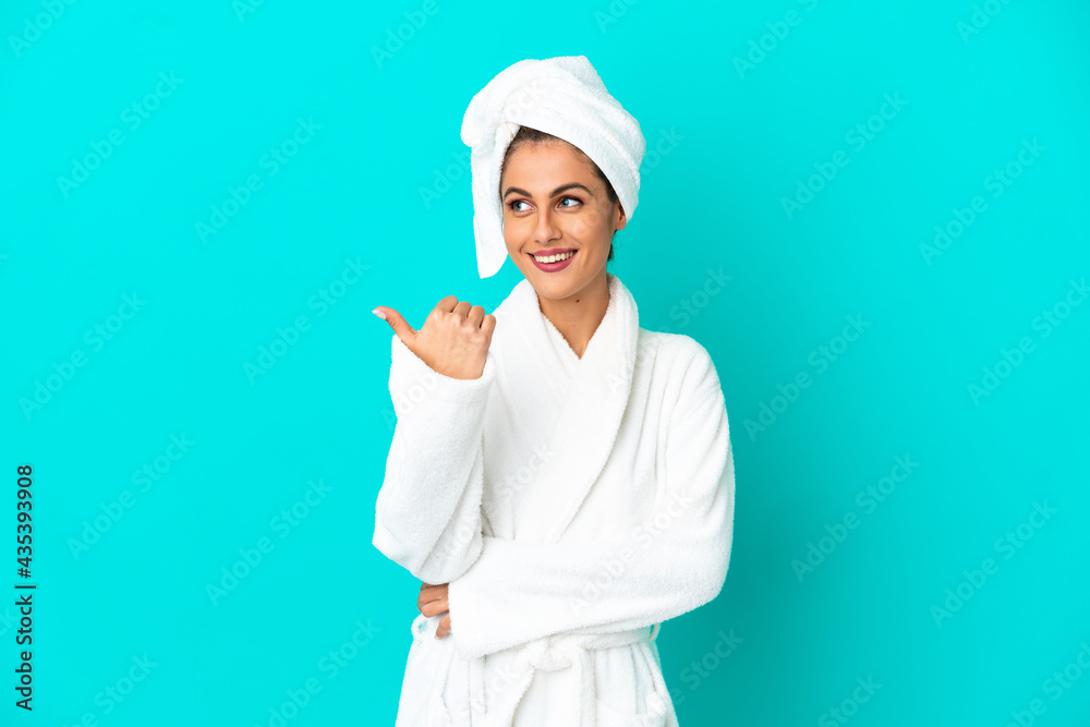Young woman in a bathrobe over isolated blue background pointing to the side to present a product Young woman in a bathrobe over isolated blue background pointing to the side to present a product