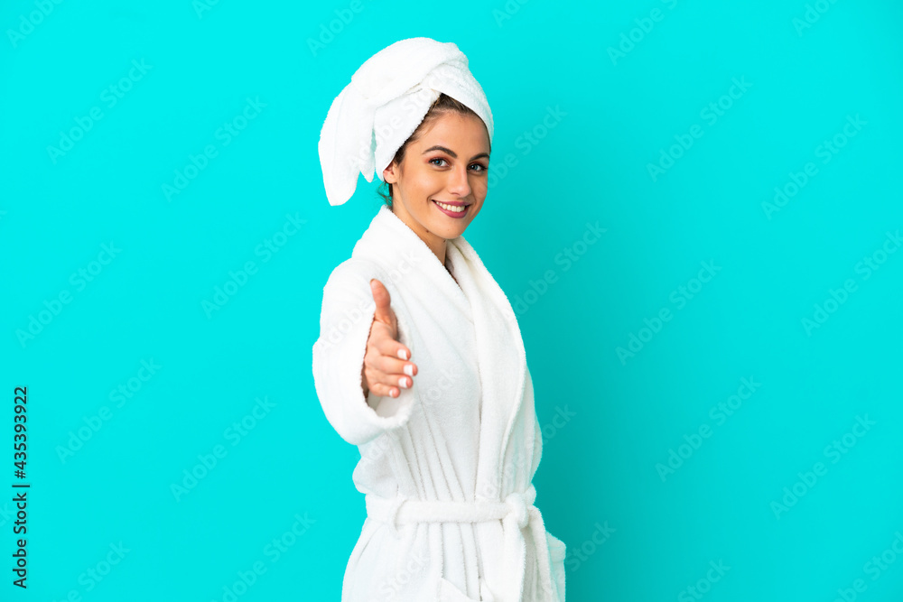 Young woman in a bathrobe over isolated blue background shaking hands for closing a good deal - obrazy, fototapety, plakaty 
