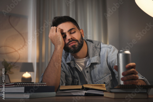 Obraz na plátně Tired young man with energy drink studying at home