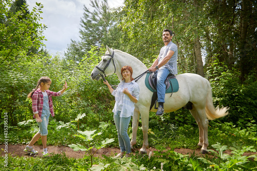 Kirov, Russia - August 07, 2020: A family including a mother, father and daughter walks and rides a horse in nature among green trees. Man, woman, girl with horse in nature in summer