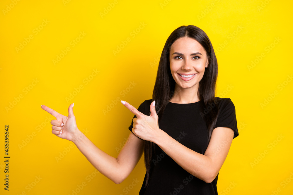 Obraz premium Photo of positive lady indicate forefingers empty space toothy smile wear black t-shirt isolated yellow color background