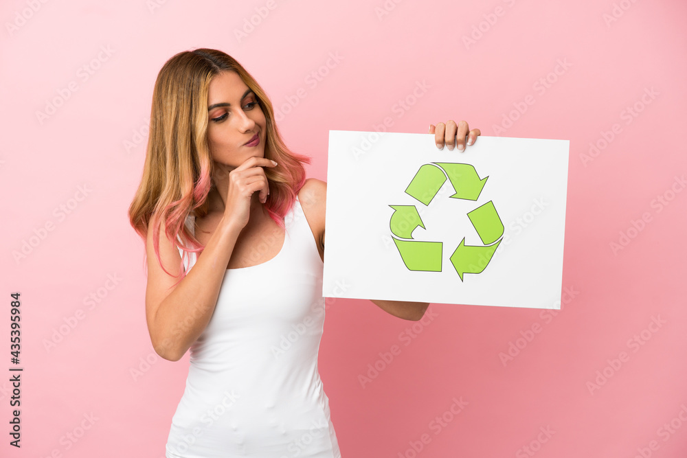 Young woman over isolated pink background holding a placard with recycle icon