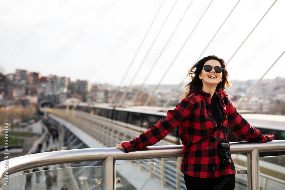 Young woman tourist standing with photo camera on the bridge. Beautiful woman traveling around the city...