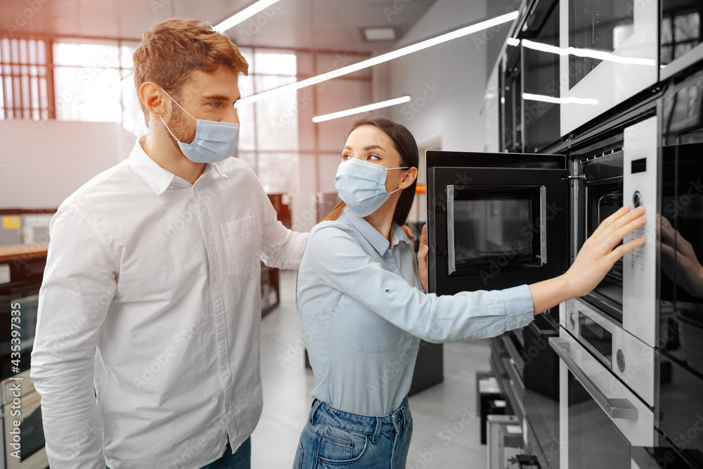 Naklejka premium Young couple wearing medical masks in hypermarket with home appliances