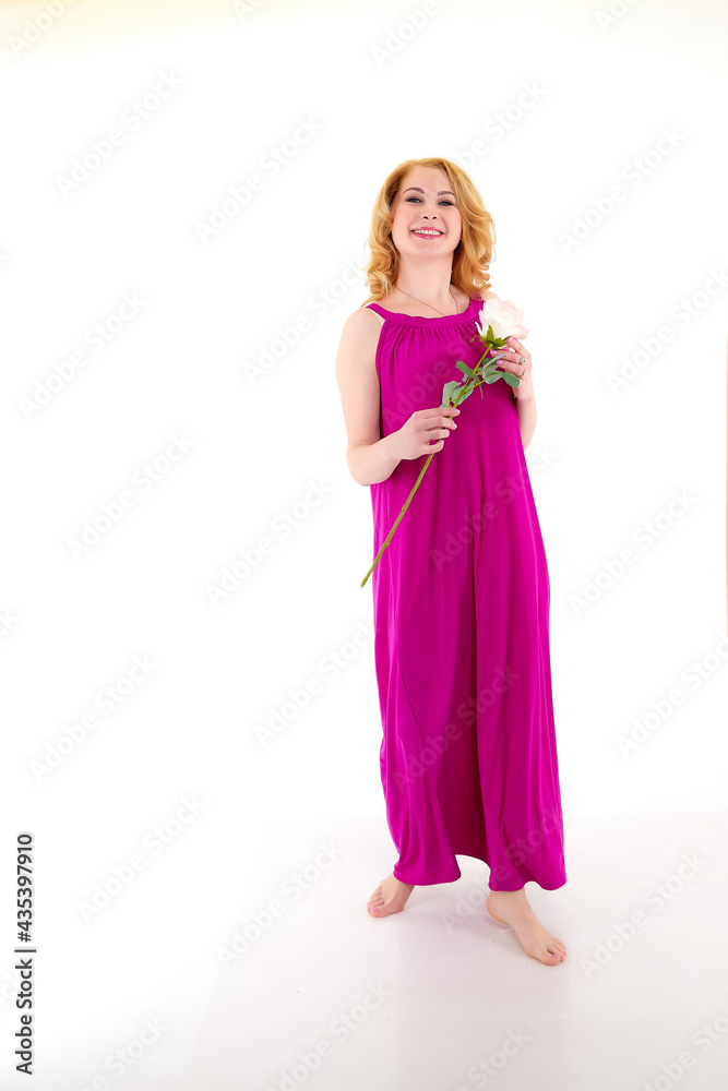Happy beautiful woman with long blond curly hair and in elegant dress posing with rose flower in studio on white background
