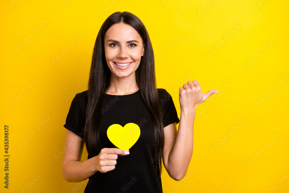 Photo of charming cheerful lady hand hold small heart card direct thumb empty space isolated on yellow color background Photo of charming cheerful lady hand hold small heart card direct thumb empty space isolated on yellow color background