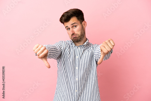 Young caucasian handsome man isolated on pink background showing thumb down with two hands