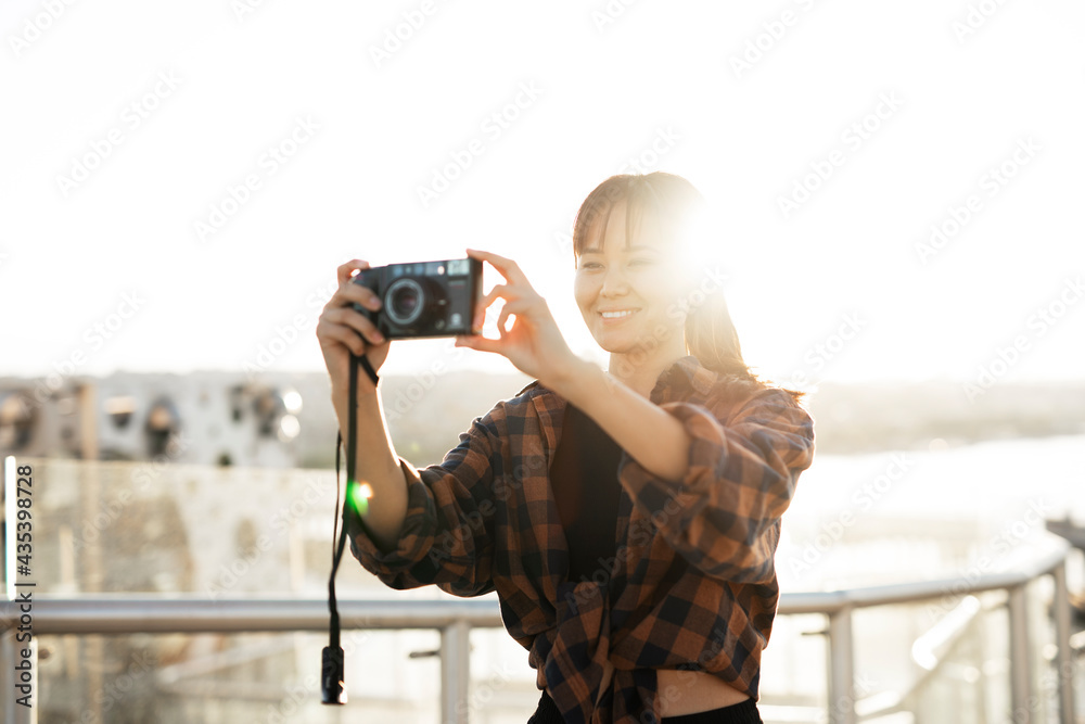 Fototapeta premium Attractive tourist with a camera. Beautiful woman with camera taking photos of beautiful location.