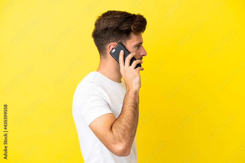 Young caucasian handsome man isolated on yellow background keeping a conversation with the mobile phone with someone Young caucasian handsome man isolated on yellow background keeping a conversation with the mobile phone with someone